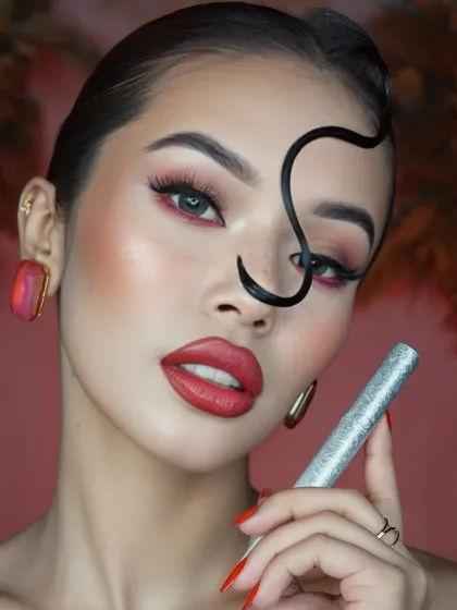 A creative shot incorporating a product, this image highlights the mascara used to achieve the fluttery lashes in this bold, artistic makeup look.