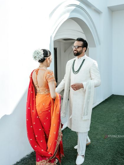 A 'first look' moment captured in Vietnam, with the groom smiling as he sees his bride in her beautiful orange and red wedding saree.