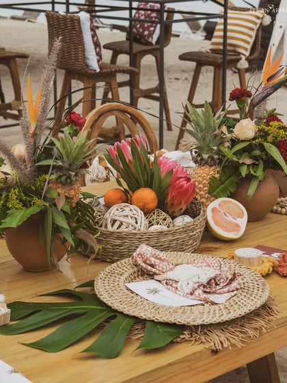 A table setting featuring woven placemats, tropical flowers like birds of paradise, and fresh fruit, fully immersing guests in the island theme.