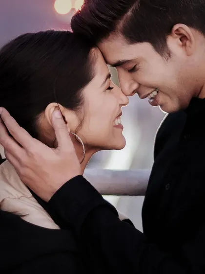 A close-up, intimate portrait that focuses entirely on the couple's connection. The soft city lights in the background create a beautiful bokeh, highlighting their smiles and the quiet moment they share. This is all about capturing raw emotion.