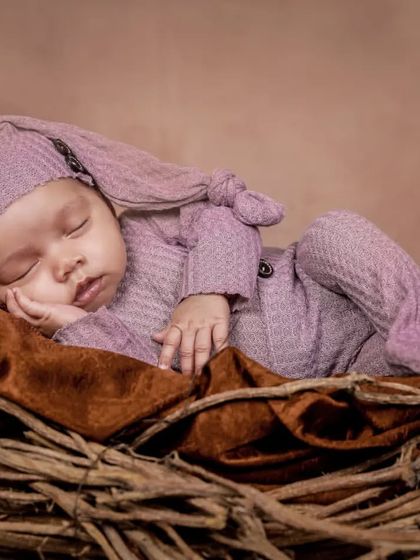 Nestled in a cozy bird's nest prop, this newborn is dressed in a soft lavender outfit. This pose is perfect for capturing that curled-up, sleepy look.