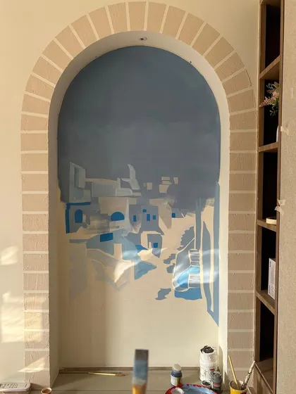 An early stage of the Santorini mural, showing the initial layers of paint that establish the composition and atmosphere of the Greek island scene.