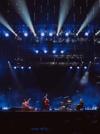 A dramatic wide shot of the Anoushka Shankar tour, with the stage bathed in brilliant blue spotlights.
