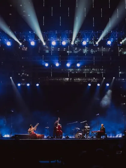 A dramatic wide shot of the Anoushka Shankar tour, with the stage bathed in brilliant blue spotlights.