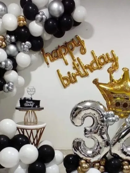 A classic black, white, and silver theme for a 34th birthday. This home decoration includes a balloon garland, 'Happy Birthday' foil letters, and large '34' foil balloons with a crown accent.