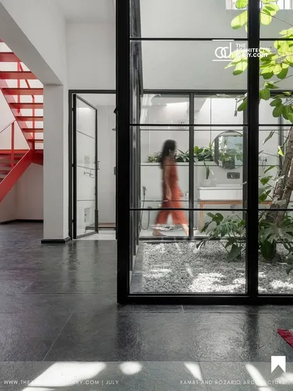 A view through the glass walls of the central courtyard, which contains a small tree and is open to the sky. This feature brings light and a piece of nature into the very core of the home, connecting multiple spaces.