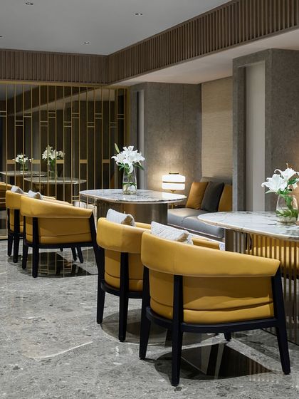 The mezzanine seating area at the Blue Sea Banquet, featuring vibrant yellow chairs and intimate table setups. A decorative metal screen provides a sense of separation while allowing views into the main hall below.