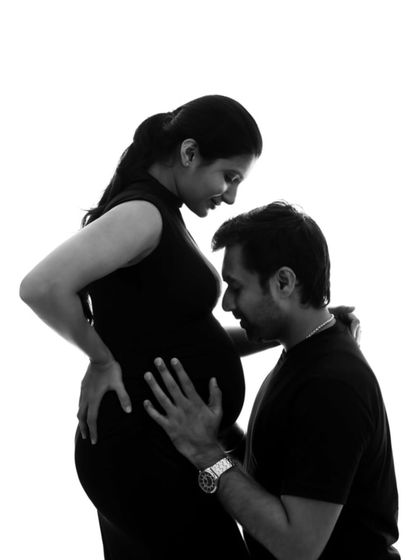 A powerful and intimate silhouette of a dad-to-be kissing his partner's belly, rendered in classic black and white.