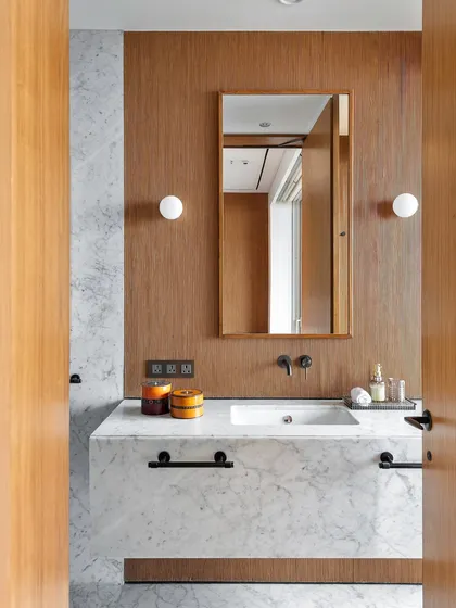 The adjoining bathroom continues the bedroom's language with minimal white Carrara marble and fluted wood accents. This visual continuity ensures a seamless transition between the sleeping and bathing areas.
