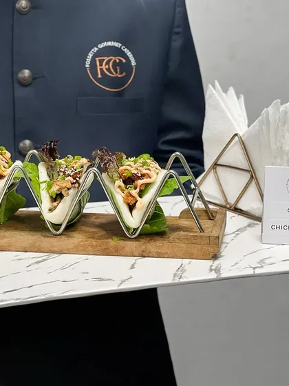 Our Crispy Chicken Bao offers a delightful textural contrast. Soft, steamed buns are filled with crispy chicken and fresh greens, presented in modern wire holders for easy handling by guests.