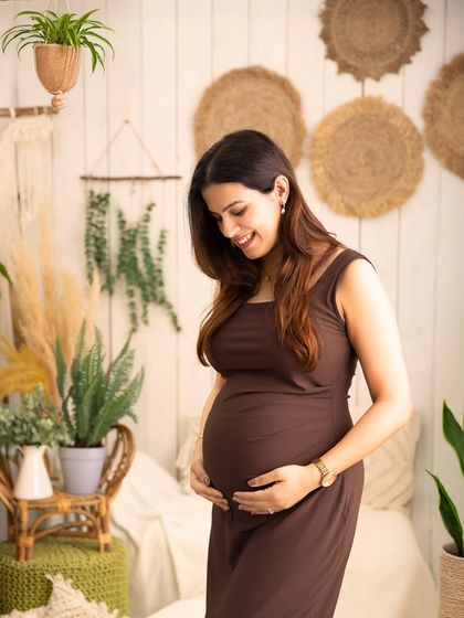 A smile that says it all. This close-up captures a moment of pure joy as the mother-to-be looks down at her belly, surrounded by the warm, bohemian decor of the studio.