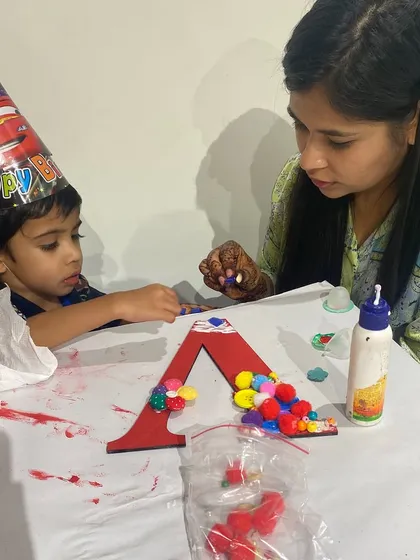 A sweet moment of concentration during a birthday party. This little boy, wearing his party hat, is carefully adding pom-poms to his initial. Monogram art is a fantastic activity for parties and playdates.