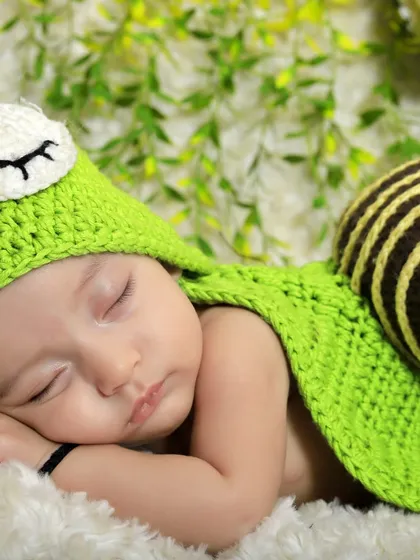I love getting creative with unique themes. This adorable shot features a baby in a hand-knitted snail costume, sleeping peacefully on a soft blanket against a leafy green background.