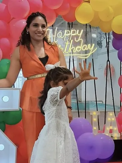 A mother and daughter celebrating a 5th birthday with custom marquee lights and a vibrant balloon arch.