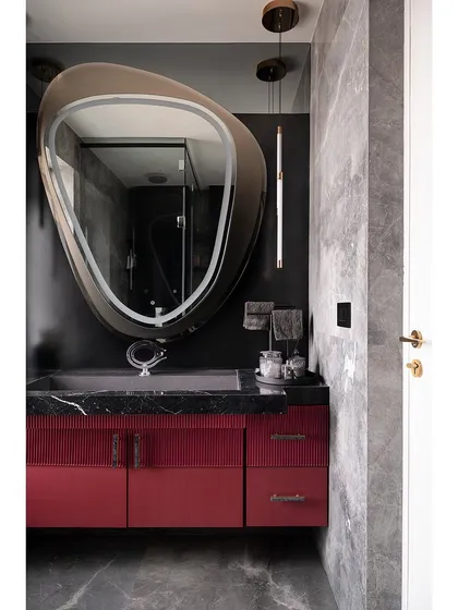 This view of the master bathroom highlights the interplay of color and texture. The deep red of the vanity, the dark grey of the walls, and the organic shape of the mirror create a space with a distinct and powerful character.