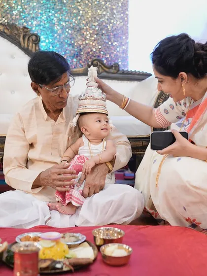 A traditional moment from the Annaprashan ceremony, with grandpa and mom placing the 'topor' on the baby's head.