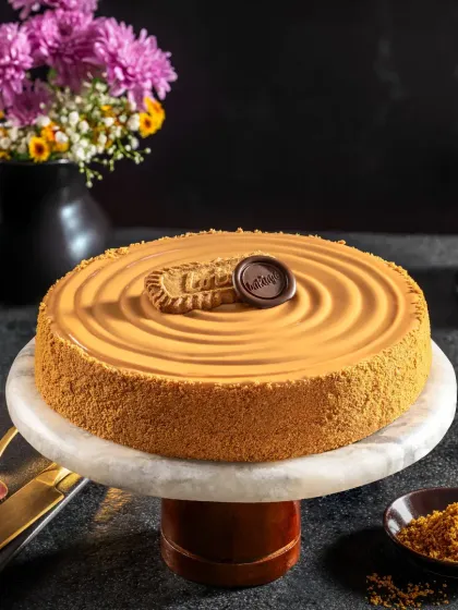 A luxurious Biscoff cheesecake on a marble stand, shot with moody, dramatic lighting that highlights its smooth texture and rich caramel tones for Bakingo.