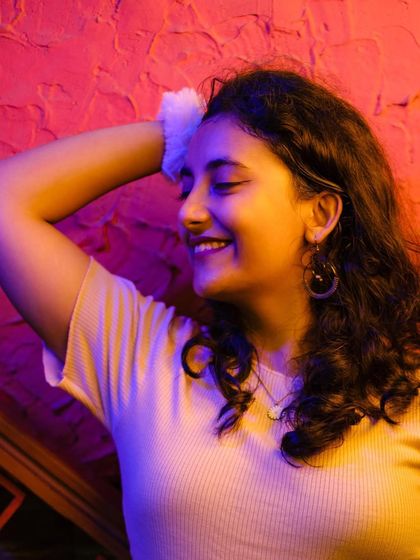 A joyful, candid portrait of a woman laughing, with her eyes closed. The soft, colorful lighting enhances the happy and relaxed mood of the moment.