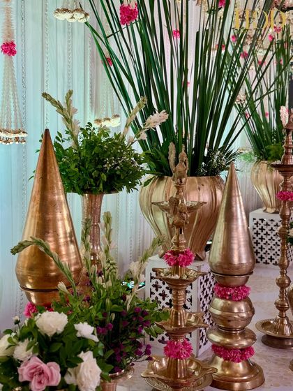 An arrangement of traditional brass and copper vessels, diyas, and fresh greenery, creating a rich and authentic feel for an engagement ceremony.