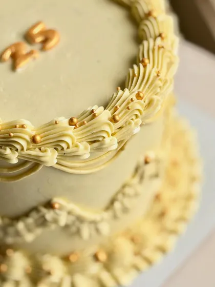A close-up of the golden vintage cake, highlighting the detailed buttercream piping and delicate gold sprinkles that give it a "golden hour" glow.