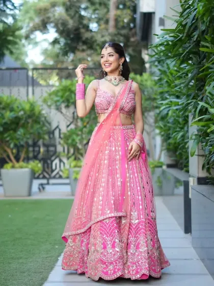 A full-length shot of a bride in a vibrant pink lehenga. The emerald and zircon choker adds a beautiful contrast, creating a look that is both fun and elegant for her special day.