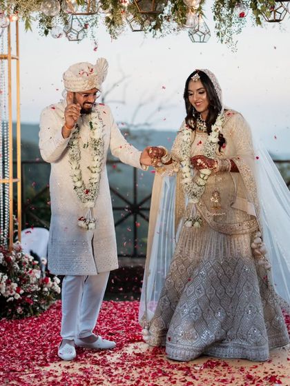 A playful moment during the varmala ceremony, with the couple sharing a laugh under a shower of rose petals.