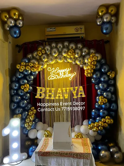 A rich blue, silver, and gold balloon arch set up in a home. This decor includes a neon sign and light-up letters for a personalized touch.
