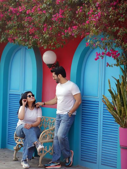A relaxed moment against a vibrant blue and red wall. This casual portrait feels like a snapshot from a romantic getaway, full of color and personality.