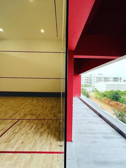 The squash court at 'The Treehouse' is placed adjacent to an open-air corridor. This 'inside-out' design allows players to easily step outside for fresh air and connects the indoor sport facility with the building's exterior environment.