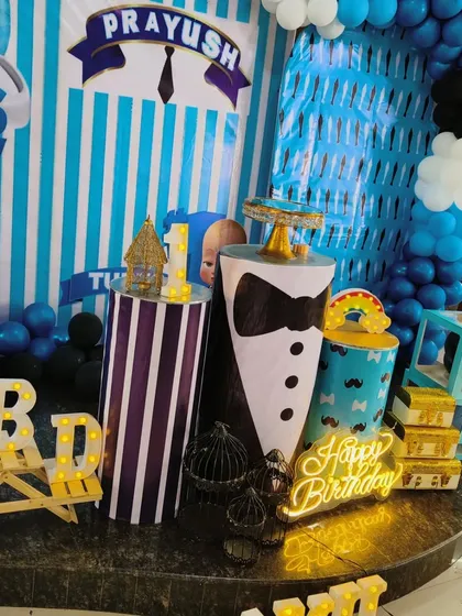 A close-up detail shot of the Boss Baby themed party. This image shows the custom-wrapped pedestals, including one designed like a tuxedo, and the 'Happy Birthday' neon sign.