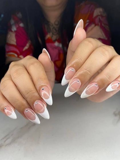 Sharp and sophisticated. This look features long, stiletto-shaped extensions with a clean French tip, accented with a single tiny rhinestone at the base of each nail.