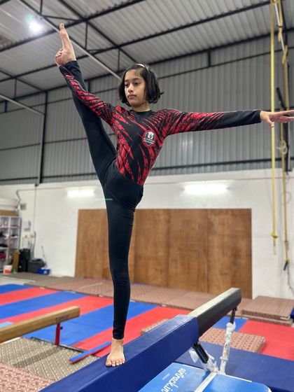 A young gymnast holds a beautiful scale on a low beam, demonstrating excellent balance and flexibility.