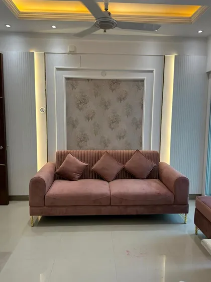 A wider view of the living room, showing how the feature wall with its integrated lighting and wallpaper panel becomes the central focus. The cove lighting in the false ceiling adds another layer of ambient light, creating a warm and inviting environment perfect for relaxing.