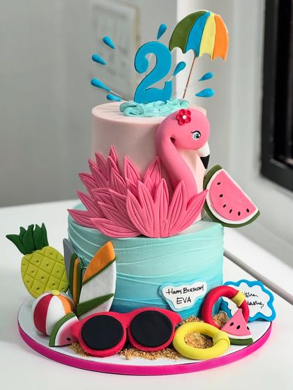 A tropical twist for turning two! This vibrant flamingo-themed cake is packed with summer fun, from fondant pineapples and watermelons to sunglasses and a cheerful flamingo centerpiece.