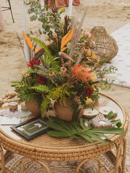 A centerpiece of exotic flowers and dried grasses on a wicker table, perfectly capturing the 'Rustic Tropics' aesthetic.