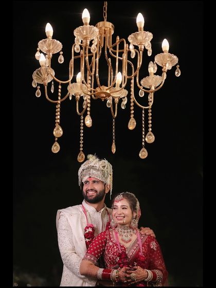 A grand and royal wedding portrait of the couple standing beneath a magnificent crystal chandelier. This shot captures the opulence of the celebration and the couple's regal presence.