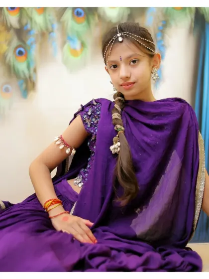 An elegant portrait of a young girl dressed as Radha. We provide beautiful traditional attire and accessories to create a graceful and timeless image against a peacock feather background.
