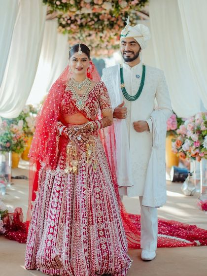 The full wedding day look. The bride stands confidently in her magnificent red lehenga, with makeup and hair styled to perfection for her grand entrance.