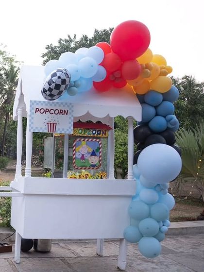 A classic popcorn cart decorated with a colorful balloon garland for the race car party.
