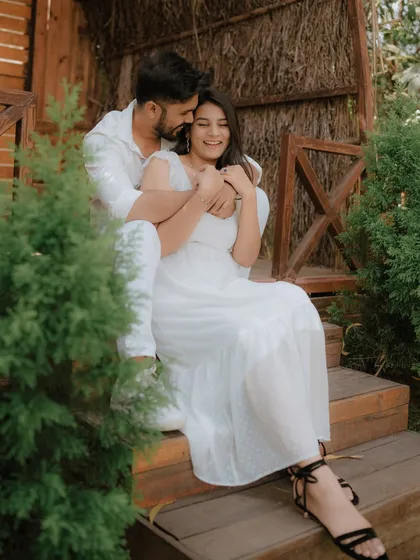 A moment of pure, uninhibited laughter on a rustic wooden porch. Dressed in coordinated white, this couple's joy is infectious, showcasing a perfectly candid moment from their pre-wedding shoot.