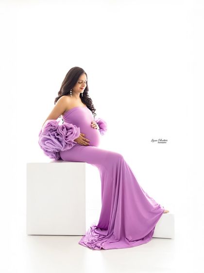 A graceful seated pose that allows the train of the lavender gown to pool beautifully. The simple white block and background keep the focus entirely on the mother-to-be.