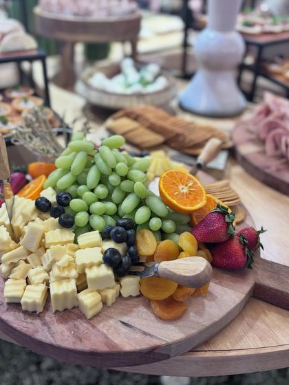 An abundant wooden cheese board overflowing with crinkle-cut cheese cubes, green grapes, dried apricots, and fresh berries. This platter is a perfect example of a generous and inviting grazing experience.