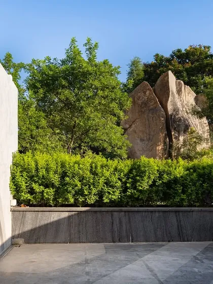 A simple office terrace transformed with landscape design. A hedge of green bushes provides a natural backdrop to a stunning rock formation, creating a peaceful escape for employees.