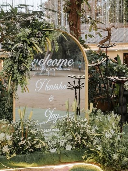 A personalized welcome sign, framed by an arch of lush greenery and unique floral light installations, creates a modern and stylish entrance for this engagement party.