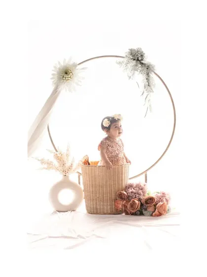 In this variation, the baby looks to the side, creating a candid and sweet profile shot within the beautifully arranged floral hoop setup. The soft lighting enhances the gentle and dreamy feel of the portrait.