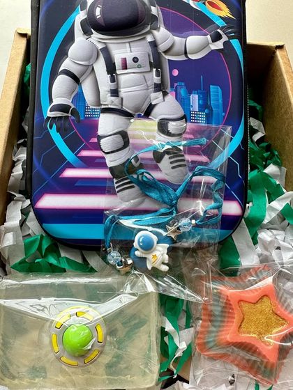 Another out-of-this-world gift box with an astronaut pencil case, a clear space-themed glycerin soap, and a star soap.