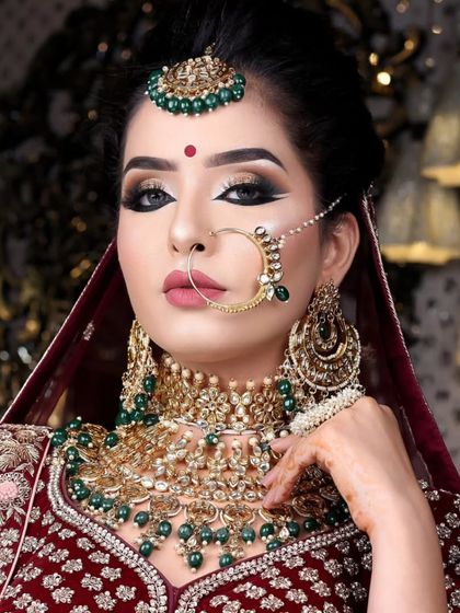 A striking bridal portrait featuring a bold Kundan and emerald green jewellery set. The dramatic eye makeup is perfectly complemented by the choker, nath, and maang tikka.