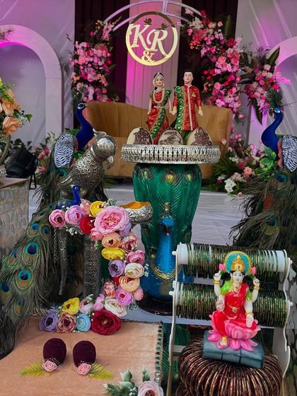 A close-up of the colorful offering table for a modern engagement, featuring peacock props and a Lakshmi idol.