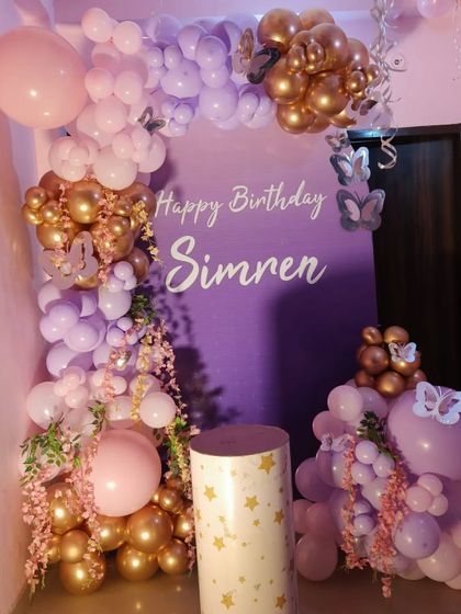 An elegant butterfly theme with a purple backdrop personalized with the name "Simren". The balloon arrangement uses shades of lavender and rose gold, with delicate butterfly and floral accents.