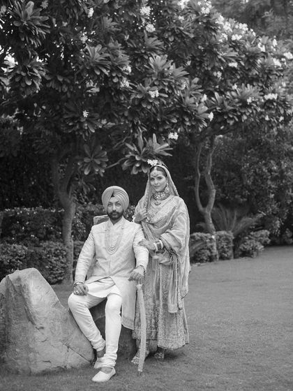 A timeless black and white portrait of a Sikh couple, posing with regal elegance in a garden setting.
